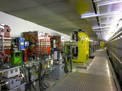 Blick entlang des Speicherrings PETRA III mit Ablenkmagneten (blau), Fokussiermagneten (rot) und Undulatoren (gelb) im Bereich der Experimentierhalle.